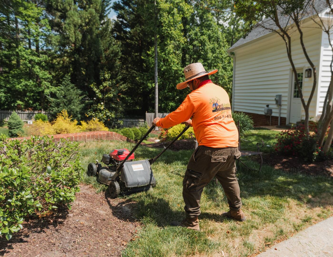 A crew member in a YardMasters shirt mowing along a bed with a walk-behind mower