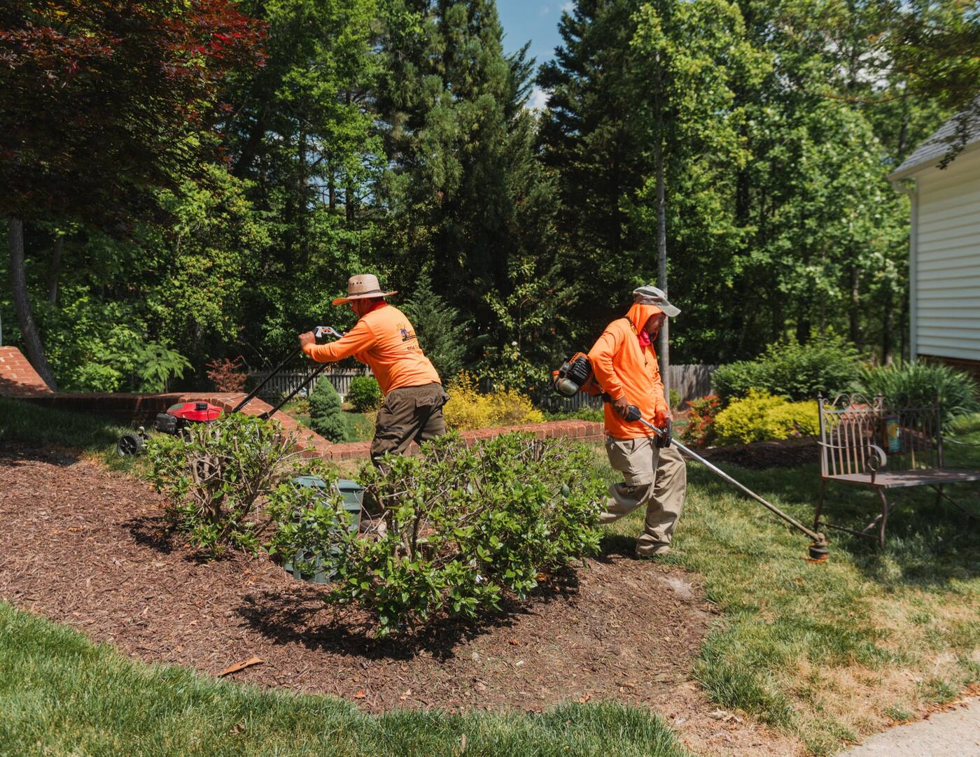 Two crew members working a planted bed, one trimming the edge