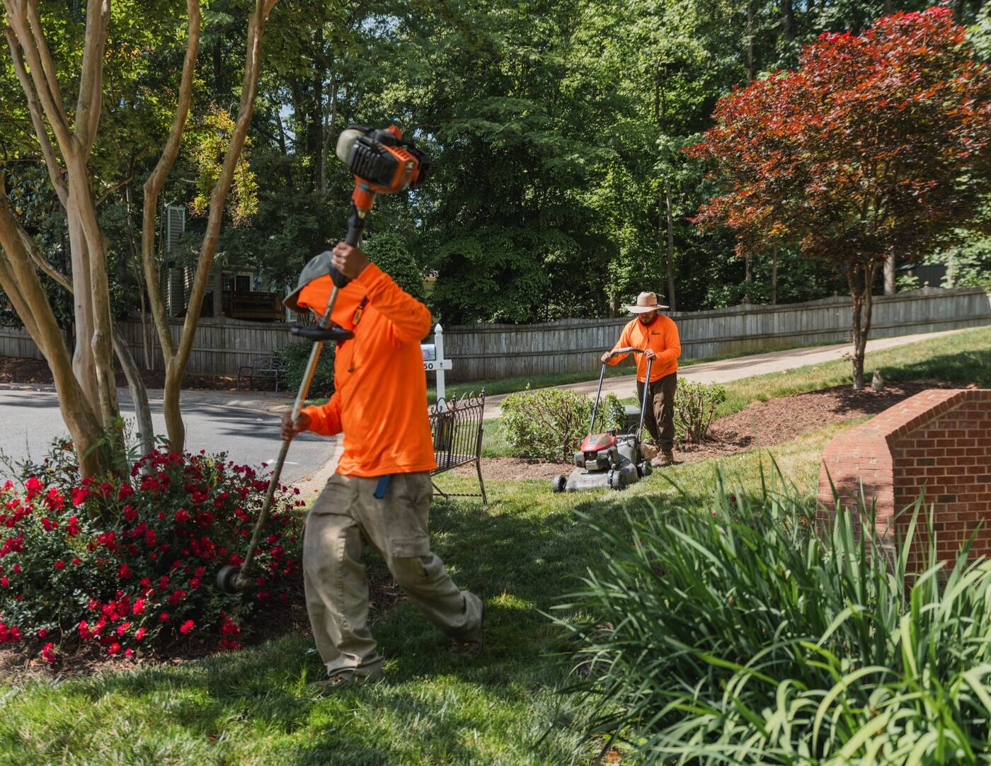 A crew member clearing a bed with a backpack blower while another mows behind